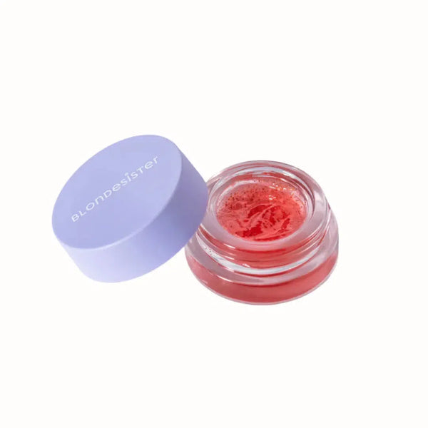 
A Blondesister lip balm in a small glass jar, featuring a soft pink tint and a smooth, jelly-like texture. The balm is housed in a purple, branded lid with the Blondesister logo, providing hydration and a natural gloss to the lips. The formula is designed for nourishing care and a subtle, glossy finish.