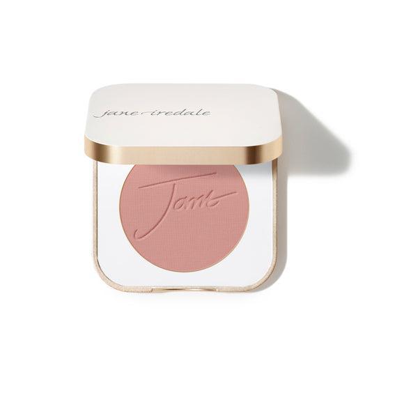 Jane Iredale Blush  
A compact case of Jane Iredale blush featuring a soft peachy-pink powder with the brand's name embossed on the surface. The compact is square-shaped with a gold trim and contains a generous amount of product.