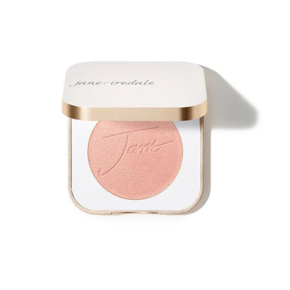 Jane Iredale Blush  
A compact case of Jane Iredale blush featuring a soft peachy-pink powder with the brand's name embossed on the surface. The compact is square-shaped with a gold trim and contains a generous amount of product.