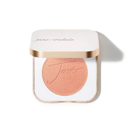 Jane Iredale Blush  
A compact case of Jane Iredale blush featuring a soft peachy-pink powder with the brand's name embossed on the surface. The compact is square-shaped with a gold trim and contains a generous amount of product.